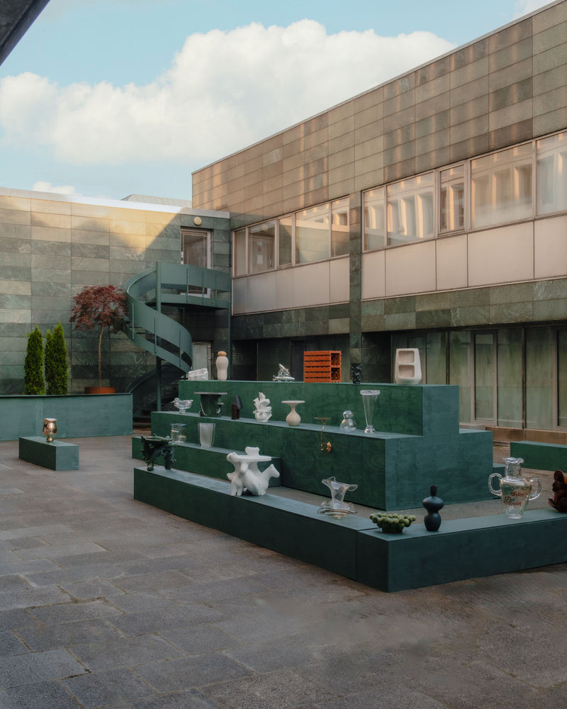 Edition Solenne exhibition with various artistic objects on green display tiers