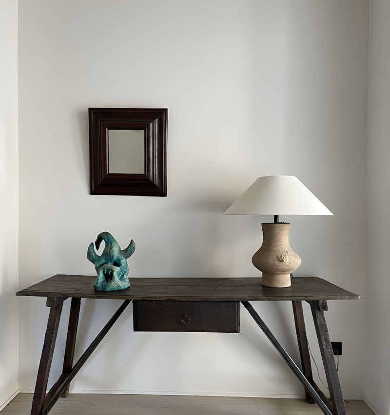 Art piece, lamp, and mirror on a rustic wooden table