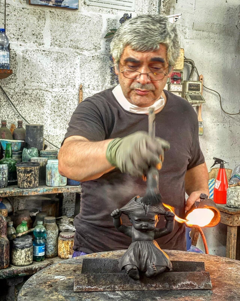 Craftsman applies flame to a dark sculpture of a child in a workshop.